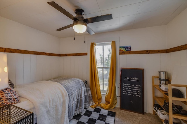 carpeted bedroom with a wainscoted wall and a ceiling fan