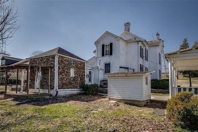 back of property featuring a chimney and an outdoor structure