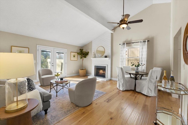 living room with french doors, light wood-style floors, a fireplace, baseboards, and vaulted ceiling with beams