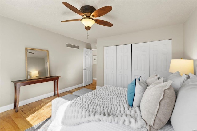 bedroom with baseboards, visible vents, light wood finished floors, ceiling fan, and a closet