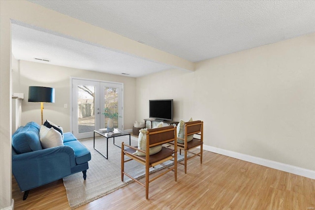 living room featuring french doors, baseboards, a textured ceiling, and light wood finished floors