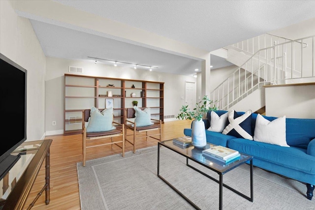 living area with visible vents, a textured ceiling, wood finished floors, stairway, and baseboards