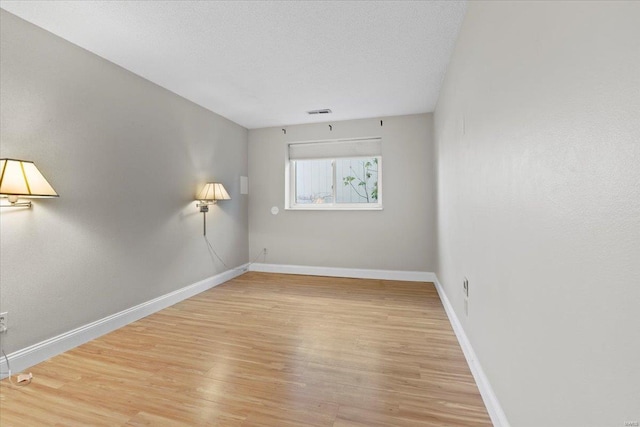 unfurnished room with visible vents, wood finished floors, baseboards, and a textured ceiling