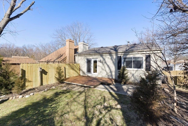 back of house featuring stucco siding, a lawn, fence, a wooden deck, and a chimney