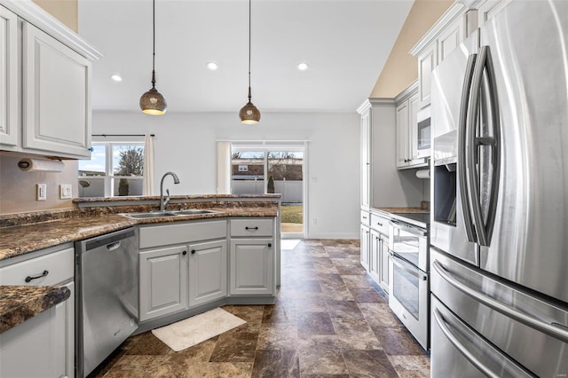 kitchen featuring decorative light fixtures, appliances with stainless steel finishes, stone finish flooring, white cabinets, and a sink