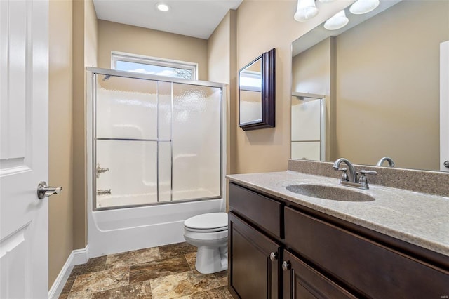 bathroom with toilet, stone finish flooring, enclosed tub / shower combo, vanity, and baseboards