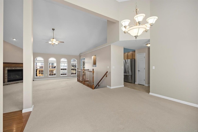 unfurnished living room with ceiling fan with notable chandelier, high vaulted ceiling, carpet floors, and baseboards