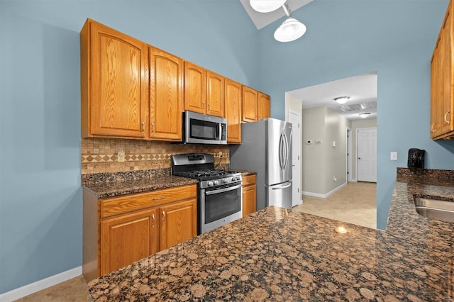 kitchen featuring appliances with stainless steel finishes, dark stone counters, baseboards, and tasteful backsplash