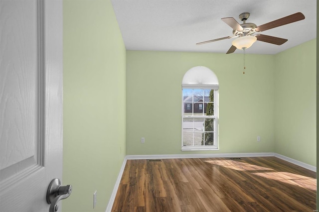 empty room featuring a ceiling fan, visible vents, baseboards, and wood finished floors