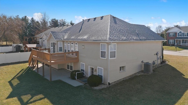 rear view of property featuring central air condition unit, a shingled roof, a lawn, fence, and a wooden deck