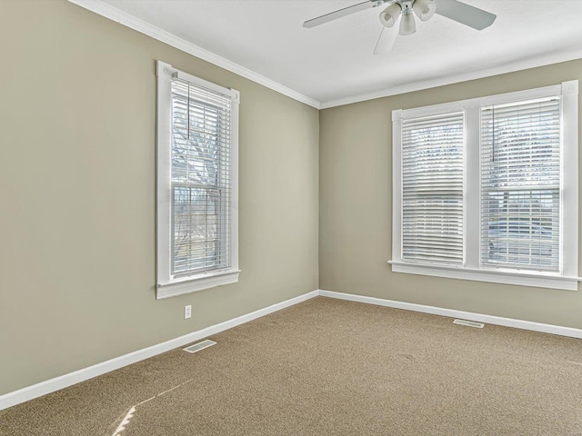 carpeted spare room with ceiling fan, visible vents, baseboards, and ornamental molding