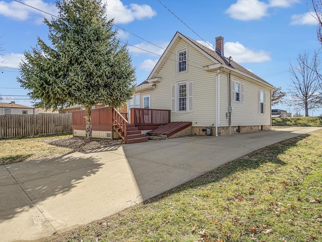 rear view of property featuring a lawn, a chimney, fence, a deck, and a patio area