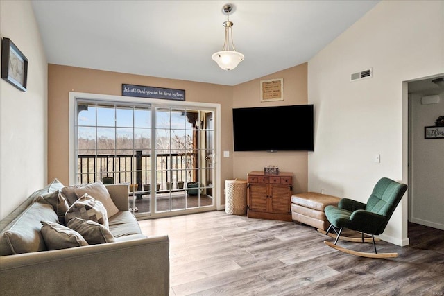 living room featuring vaulted ceiling, wood finished floors, visible vents, and baseboards