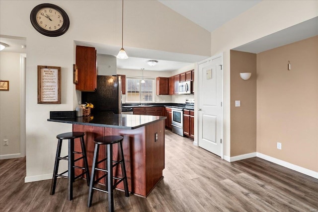 kitchen with wood finished floors, appliances with stainless steel finishes, a breakfast bar area, a peninsula, and lofted ceiling