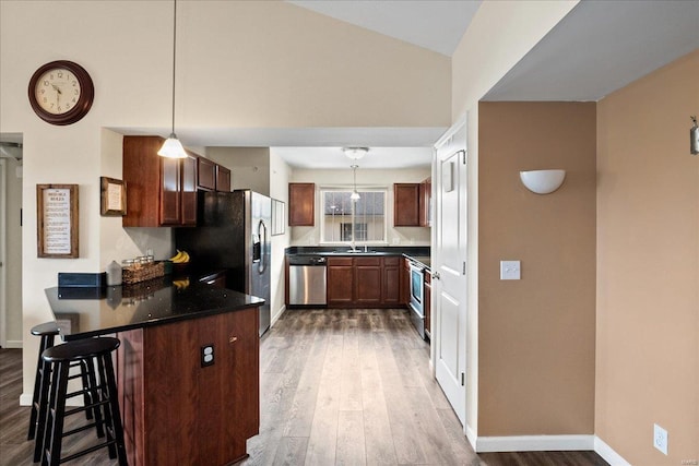 kitchen with wood finished floors, baseboards, a peninsula, stainless steel appliances, and dark countertops