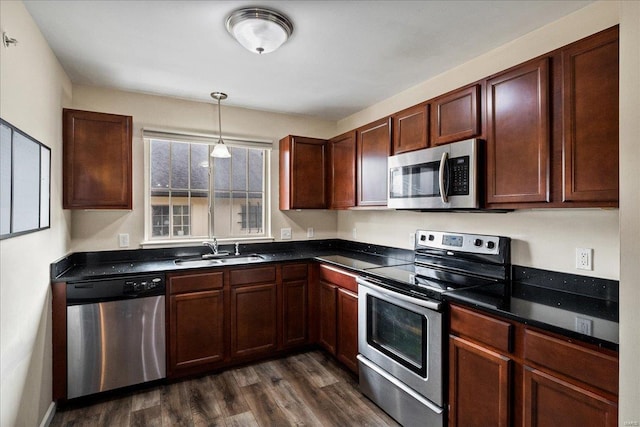 kitchen featuring a sink, hanging light fixtures, dark wood-type flooring, appliances with stainless steel finishes, and dark countertops