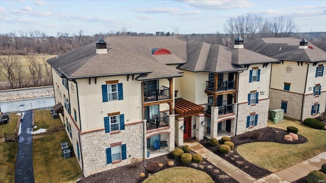 view of front facade with stone siding, stucco siding, a chimney, and a balcony