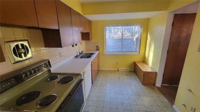 kitchen with baseboards, a sink, light countertops, backsplash, and range with electric stovetop