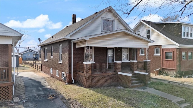 bungalow featuring covered porch, brick siding, and driveway