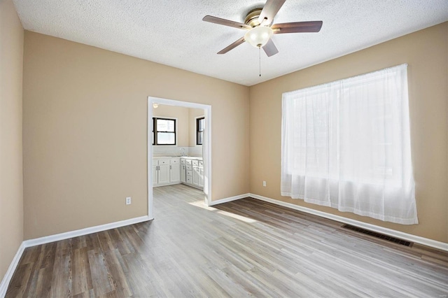 empty room with light wood finished floors, visible vents, ceiling fan, a textured ceiling, and baseboards