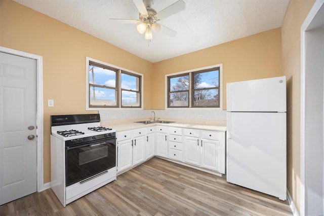 kitchen with white appliances, white cabinets, light countertops, light wood-type flooring, and a sink