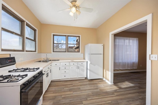 kitchen featuring white appliances, wood finished floors, a sink, white cabinets, and light countertops