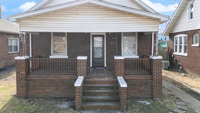 bungalow-style house featuring covered porch, brick siding, and cooling unit