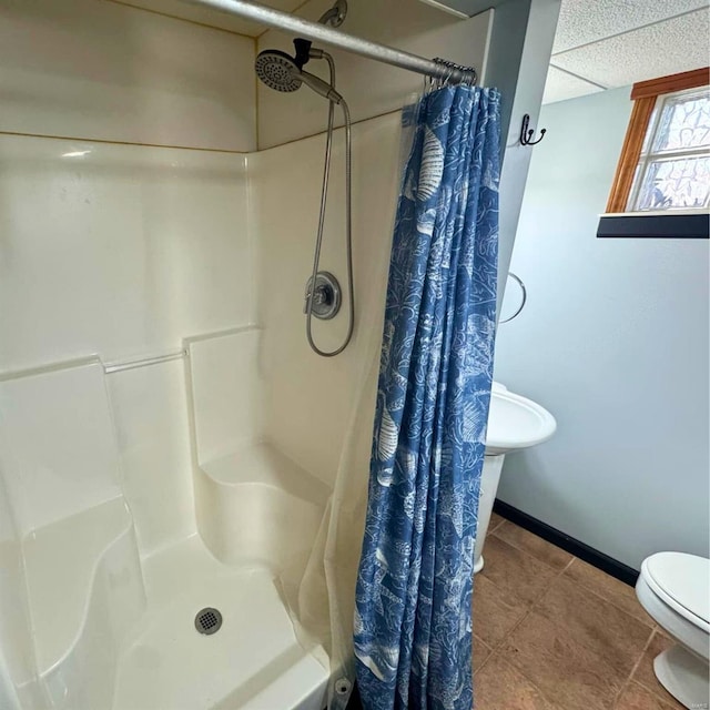 bathroom with a stall shower, baseboards, a drop ceiling, toilet, and tile patterned floors