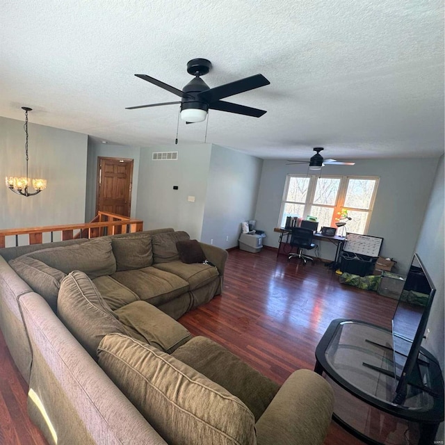 living room featuring dark wood-style flooring, visible vents, a textured ceiling, and ceiling fan with notable chandelier