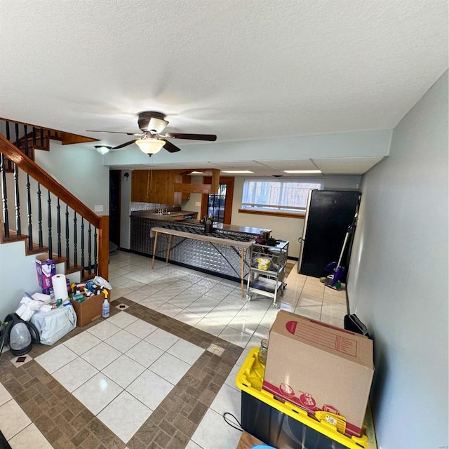 living area with light tile patterned flooring, ceiling fan, a textured ceiling, and stairs