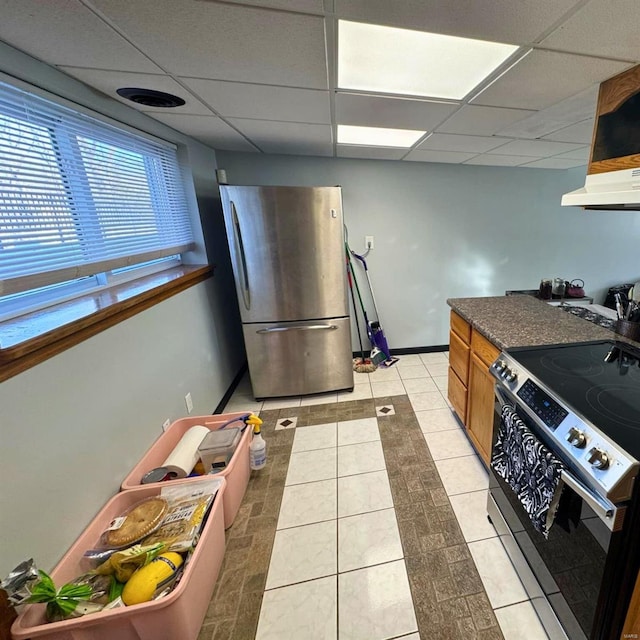 kitchen featuring appliances with stainless steel finishes, brown cabinetry, light tile patterned flooring, and a drop ceiling