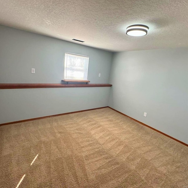 carpeted empty room featuring baseboards, visible vents, and a textured ceiling