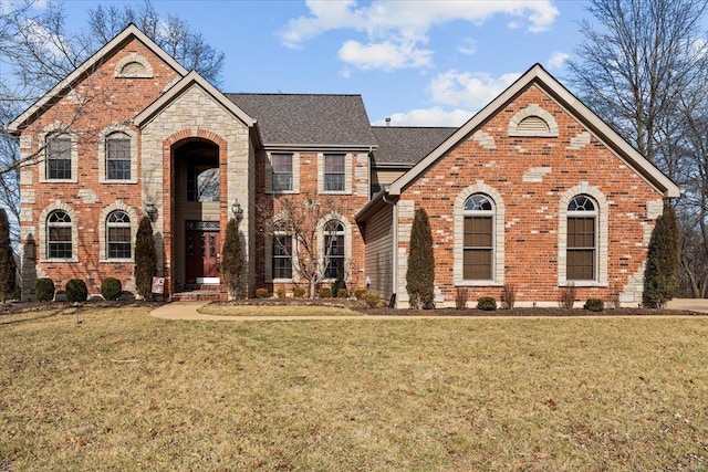 traditional home featuring a shingled roof, a front yard, and brick siding