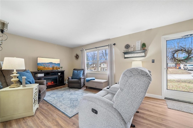 living area with light wood finished floors, a glass covered fireplace, and baseboards