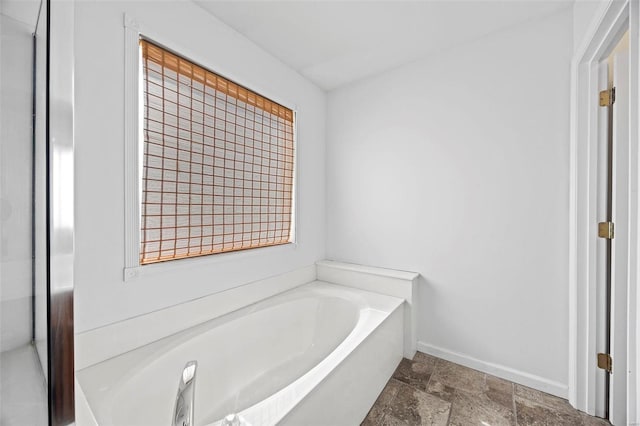 full bath featuring stone finish floor, a garden tub, and baseboards