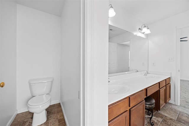 bathroom featuring toilet, stone tile floors, a sink, baseboards, and double vanity