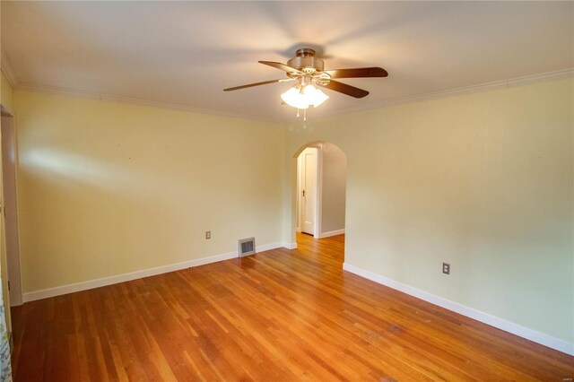 spare room featuring arched walkways, light wood finished floors, visible vents, and crown molding