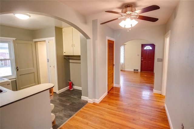 corridor with baseboards, visible vents, arched walkways, and wood finished floors