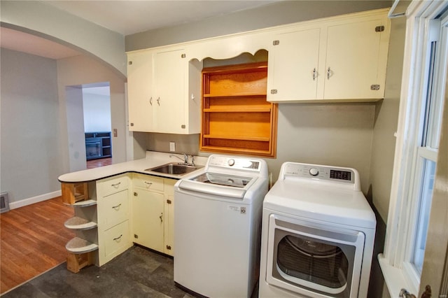 clothes washing area with cabinet space, baseboards, arched walkways, independent washer and dryer, and a sink