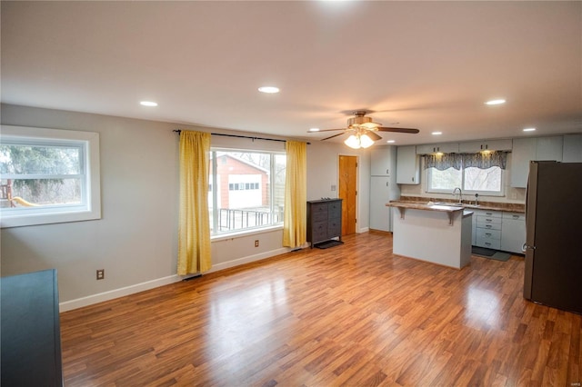 kitchen with baseboards, a breakfast bar area, wood finished floors, and freestanding refrigerator