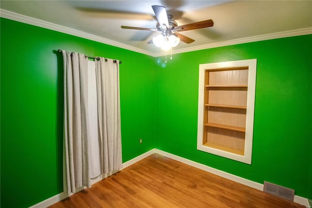 spare room featuring built in features, baseboards, visible vents, wood finished floors, and crown molding