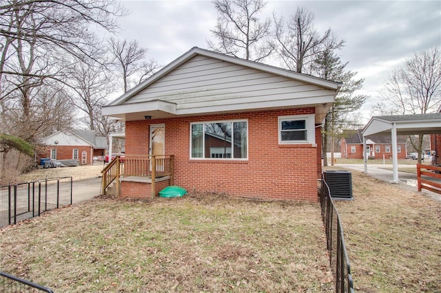 bungalow-style home with brick siding, central AC unit, fence, and a front yard