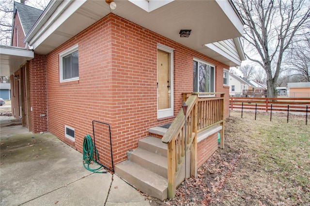 entrance to property featuring brick siding, fence, and roof with shingles