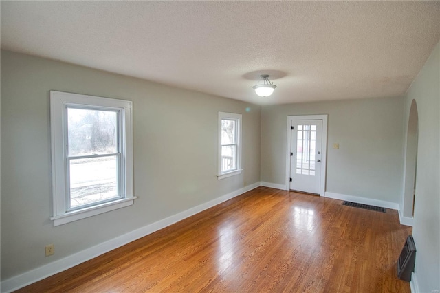 empty room featuring baseboards, visible vents, arched walkways, and wood finished floors