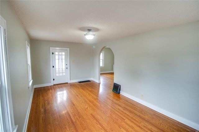 interior space featuring light wood finished floors, baseboards, arched walkways, and a textured ceiling