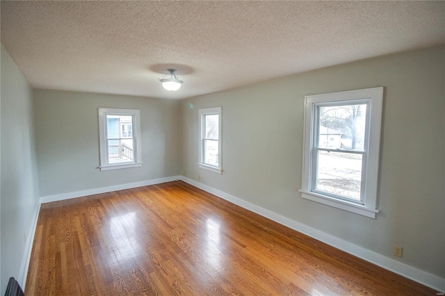 empty room featuring a textured ceiling, baseboards, and wood finished floors