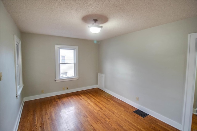 empty room featuring a textured ceiling, wood finished floors, visible vents, and baseboards