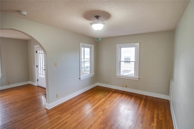 unfurnished room with arched walkways, a textured ceiling, baseboards, and wood finished floors