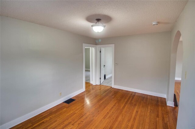 empty room with arched walkways, a textured ceiling, wood finished floors, visible vents, and baseboards