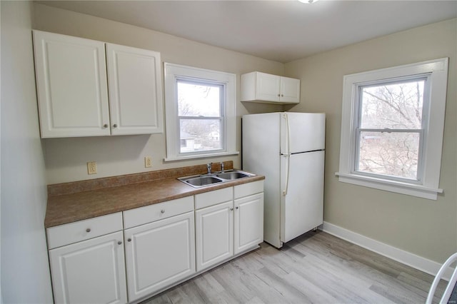 kitchen featuring baseboards, dark countertops, freestanding refrigerator, white cabinetry, and a sink